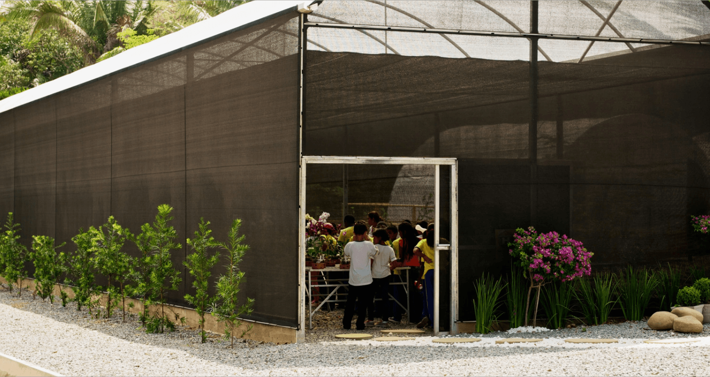 Entrada de uma estufa com flores, já possível ver que dentro do espaço há crianças