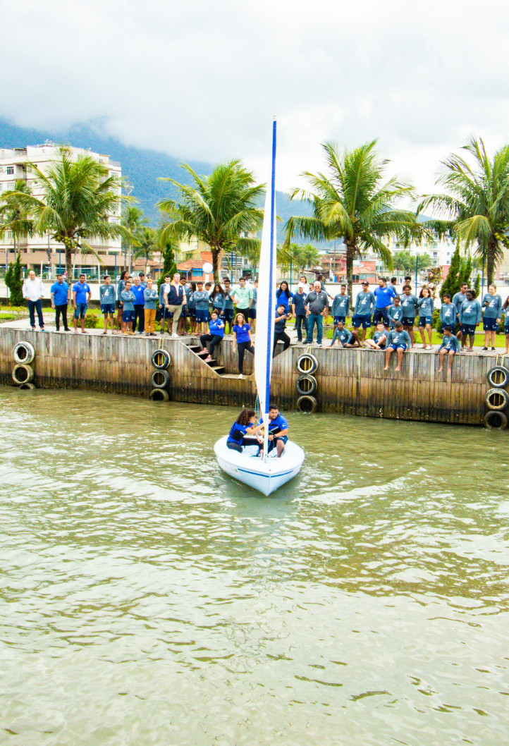 Two people are in a dinghy in the water and several people are watching them on a wall