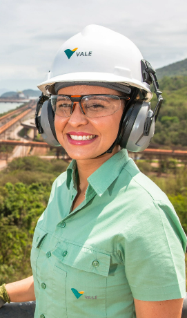 Foto de mulher branca com uniforme da Vale, óculos, capacete e proteção nos ouvidos.