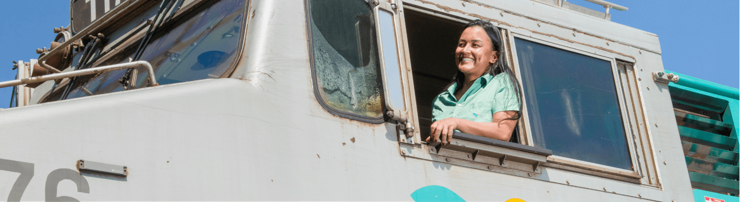 Mulher sorrindo na direção de um dos trens da Vale. Ela está usando uma camisa verde clara.