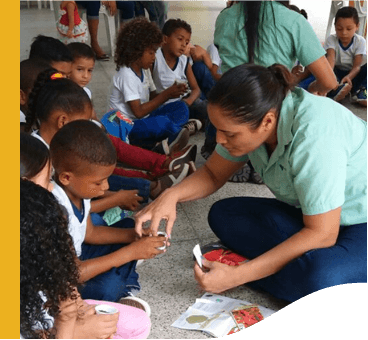 Several children are sitting on the floor, interacting with two Vale employees.