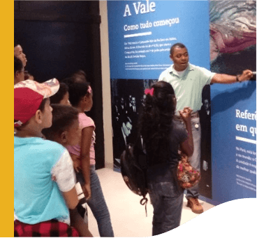 Several children are standing looking at a panel, while Vale employee explains the content.