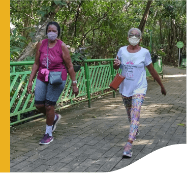 Two ladies walk through a place full of trees. Both wear protective masks.