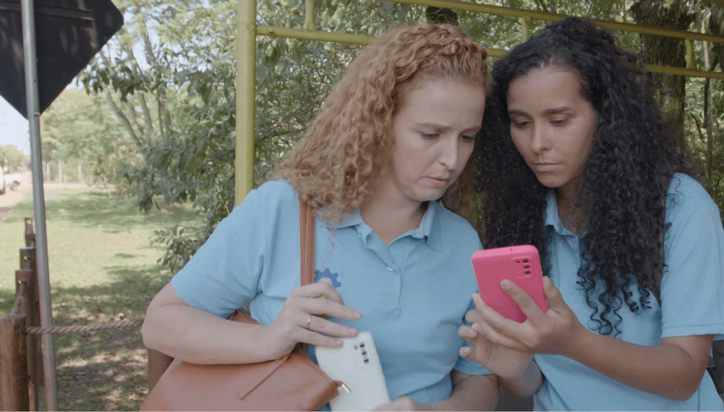 Duas mulheres paradas lado a lado olhando para um celular.