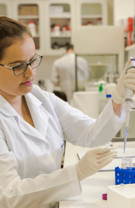 Uma cientista, de jaleco branco e luvas, manuseando um tubo de ensaio em um laboratório.
