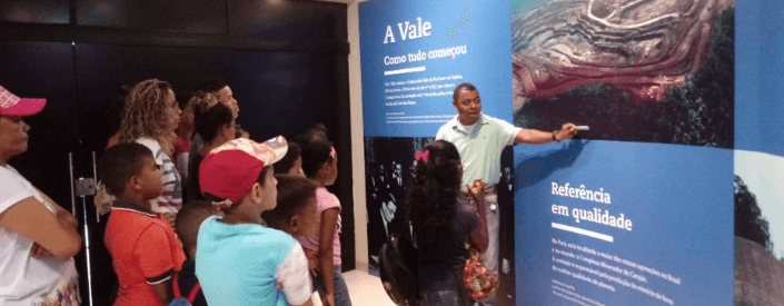 Several children are standing looking at a panel, while Vale employee explains the content.