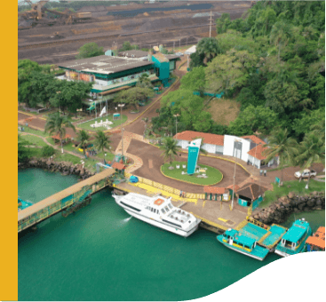 Aerial image of the Guaíba Island terminal. At the top of the image, we see an area of land on the left. On the right, a mountainous area with vegetation. In the middle there are several concrete structures, and below, you can see the water, a moored motorboat, and a kind of bridge.