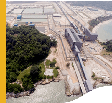 Aerial image of Teluk Rubiah Terminal. On the left is an area of vegetation, underneath you can see water, and in the rest of the image is an operation area with large equipment.