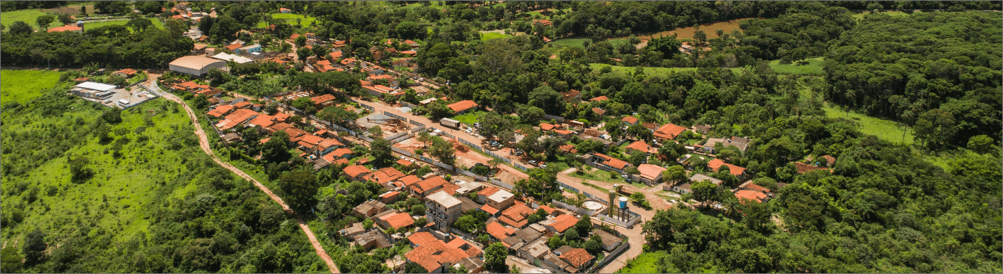 Imagem aérea de uma cidade. O local é cercado por vegetação e há muitas casas no centro.