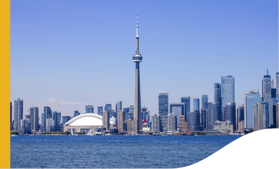 Vista de Toronto. A cidade é banhado por água e ao fundo da imagem há diversos prédios e uma grande torre ao centro