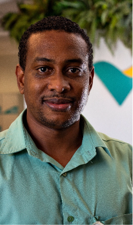 Photo of a black man in an office. He is wearing a Vale uniform, a green button-up shirt, and he has short hair.