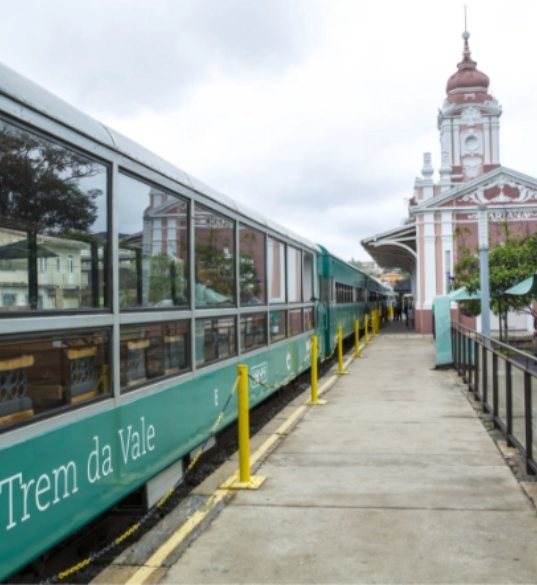 Um trem Vale está estacionado na plataforma e três pessoas, acompanhadas de malas, estão embarcando.