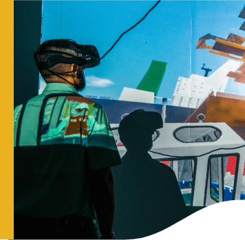 Homem de costas usando camisa verde clara e óculos tecnológicos e olhando para uma parede em que há projeções de ilustrações simulando o trabalho em portos.