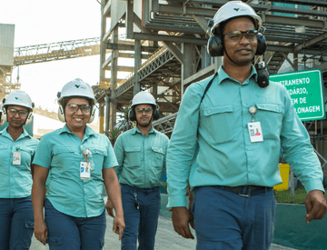 Male and female employees walking in side by side in an operation space. All are wearing green uniforms, goggles, ear muffs and white helmets with Vale logo.