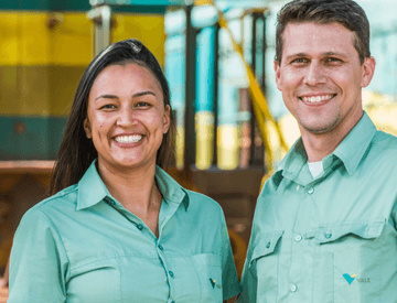 Photo taken from the waist up of two Vale employees – a man and a woman – smiling an operation space. The two wear light green shirts.