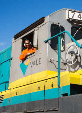 Um empregado Vale sorri para foto, dentro da cabine de um trem.