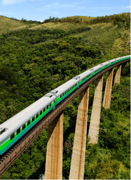 Trem Vale seguindo por uma ferrovia elevada. Em volta é possível ver uma paisagem montanhosa e repleta de vegetação.