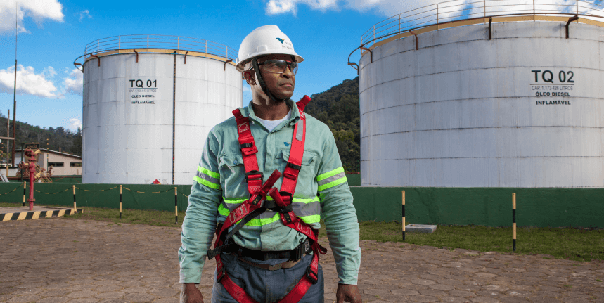 Homem negro parado em uma área de operações. Ele usa uniforme e equipamentos de proteção.