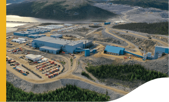 Industrial area, surrounded by mountains. In the center, there are several warehouses and dirt ground.