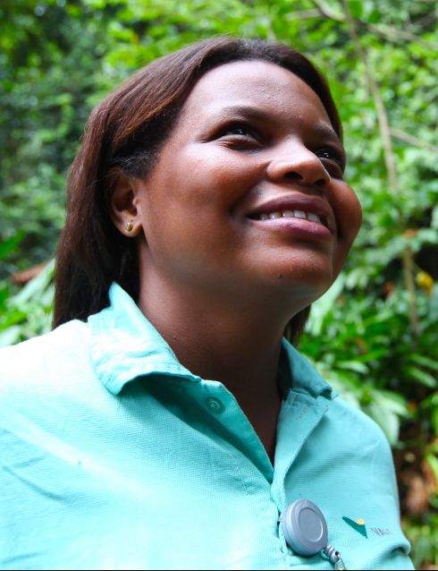Foto da altura do peito até a cabeça de uma mulher negra olhando para o alto e sorrindo, utilizando um uniforme verde da Vale, camisa verde de botão
